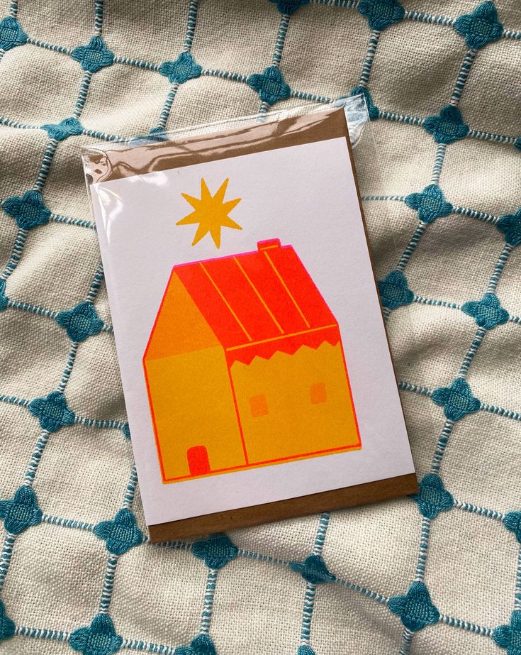 a card with a house on it sitting on top of a bed covered in blue and white fabric