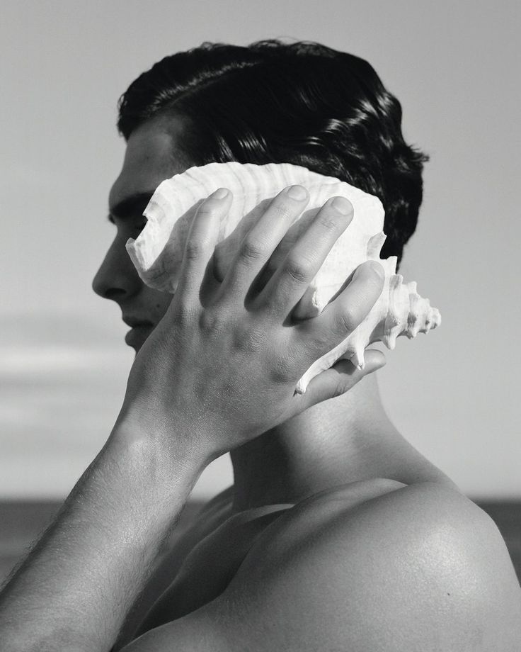 black and white photograph of a man covering his face with a piece of paper in front of him