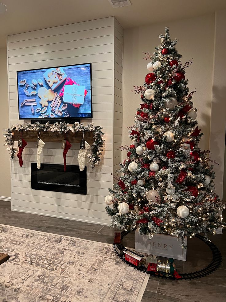 a living room with a christmas tree, fireplace and television on the wall in front of it