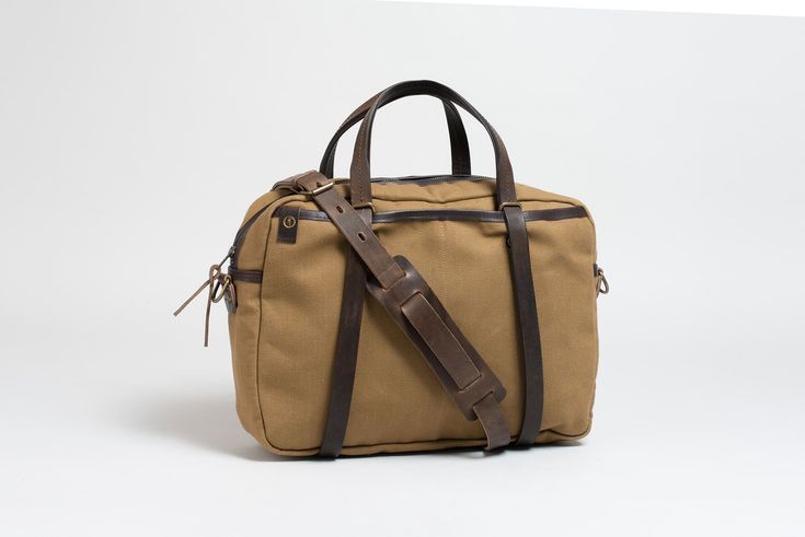 a tan canvas bag with brown leather handles and straps on the front, sitting against a white background