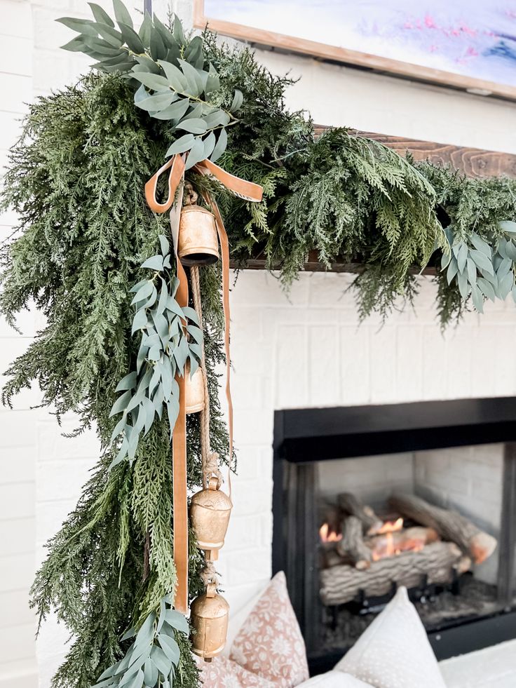 a fireplace decorated for christmas with greenery and bells