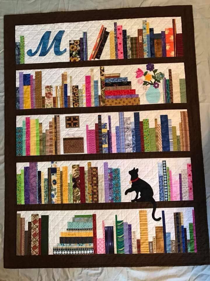 a quilted book shelf with books and a cat sitting on top of the shelves