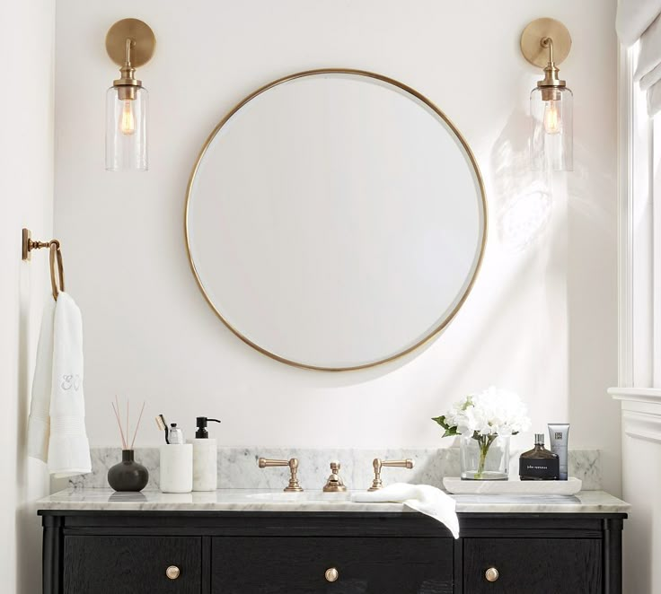 a bathroom vanity with two sinks and a round mirror on the wall above it, in front of a window