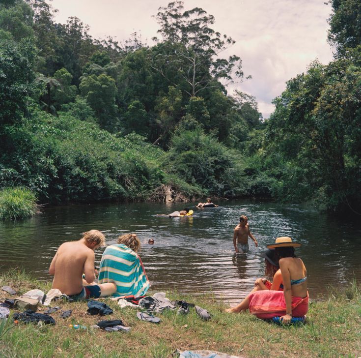 several people are sitting in the water near some trees and towels on the ground,