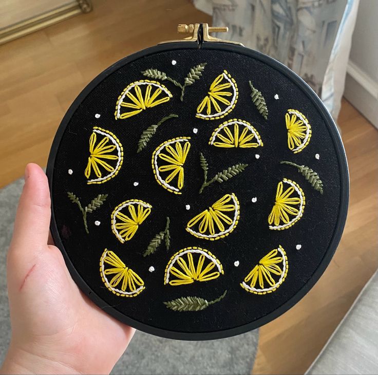 a hand holding up a black and yellow embroidered round case with gold butterflies on it