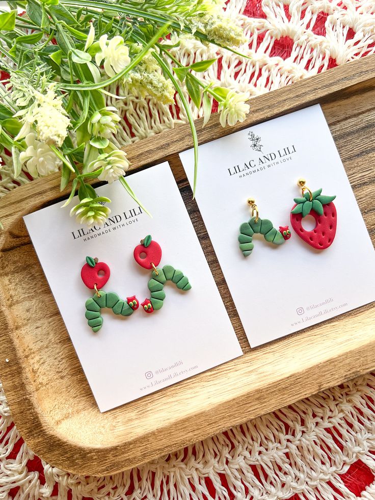 two earrings are sitting on a table next to some flowers and a vase with green leaves