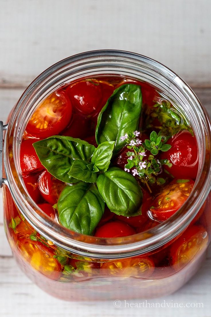 a glass jar filled with tomatoes and basil