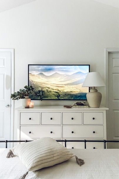 a bedroom with white furniture and a large painting on the wall above it's bed