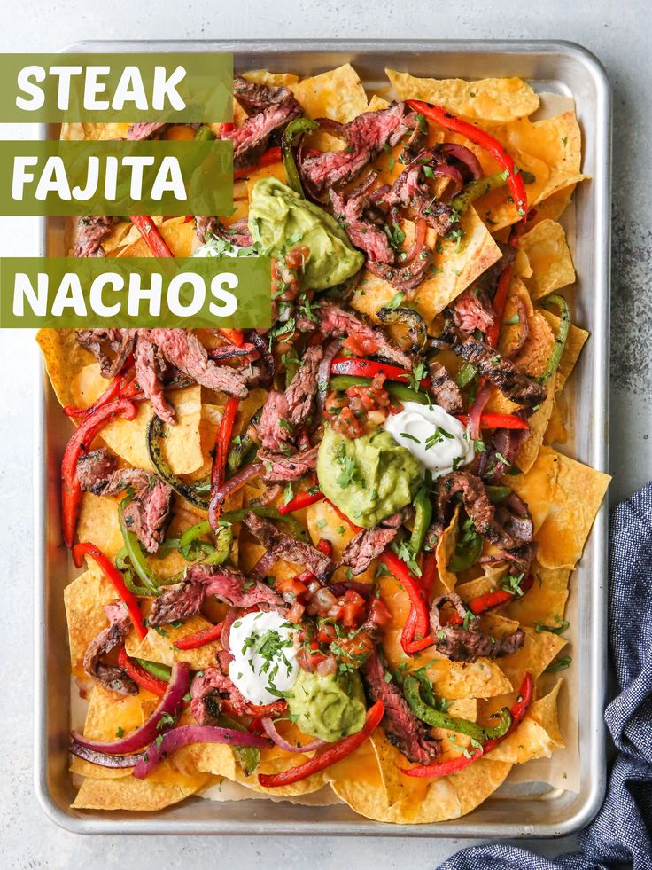 a tray filled with nachos topped with beef, peppers and guacamole