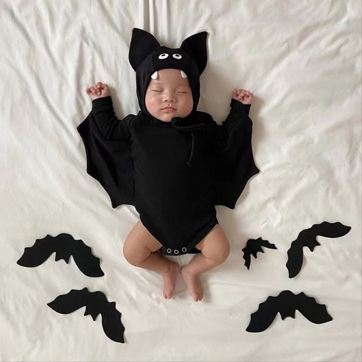 a baby wearing a bat costume laying on a bed