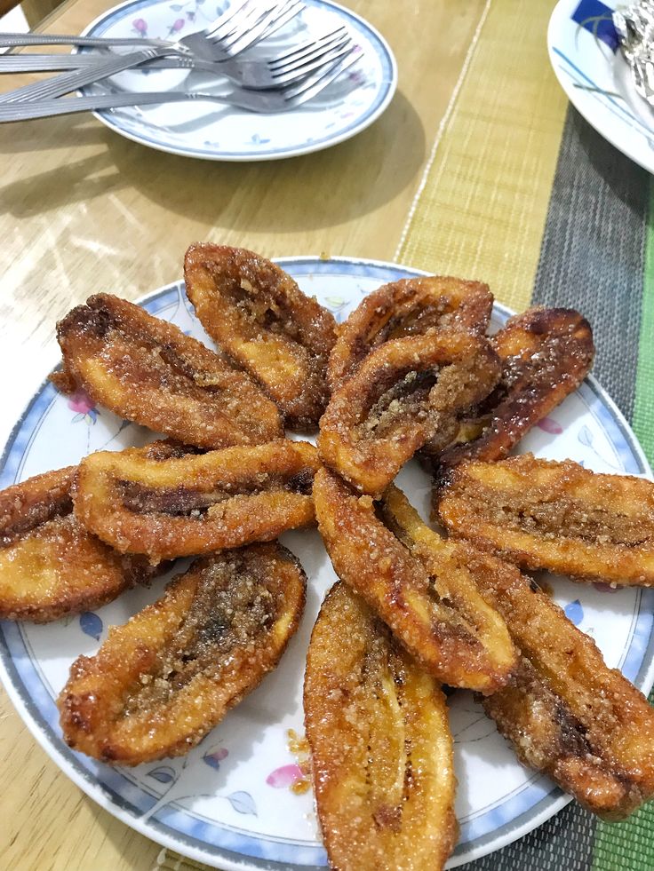 there is a plate full of fried bananas on the table with forks and spoons