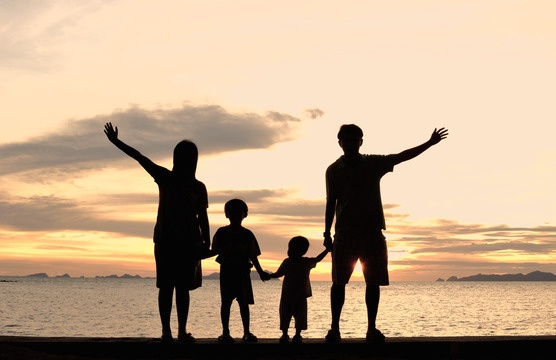 a family is standing on the beach with their arms in the air as the sun sets