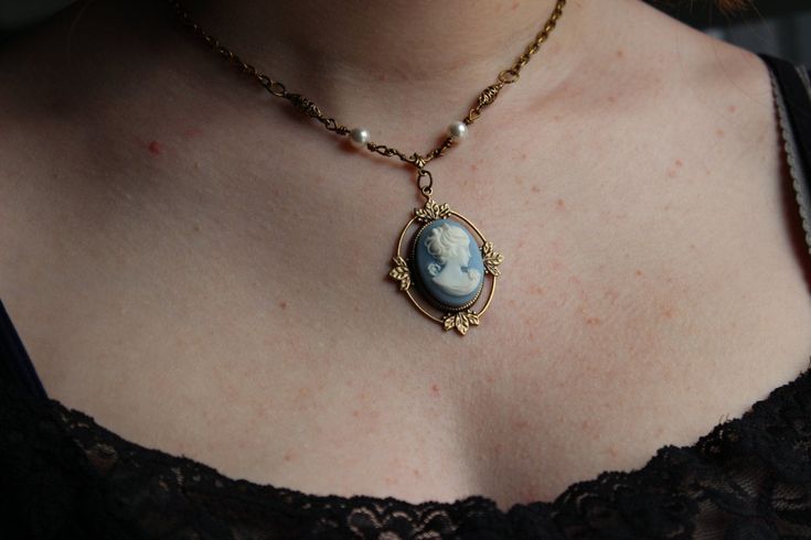 "Enchanting Blue Cameo in a lovely design called the Kathrine Necklace. Features a drop portrait cameo in a leaves embellished setting hanging from an ornate drop. Pearls and cast floral antiqued golden beads are hand linked and wire-wrapped to enhance the lovely tones and textures of this Victorian cameo. Your necklace will be finished with antiqued gold chain that is finely textured. Closure is done with our hand forged loops which are durable and allow adjustable length. You necklace has a lo Elegant Cameo Necklaces For Wedding, Elegant Cameo Necklace For Wedding, Oval Pendant Cabochon Necklace For Wedding, Oval Pendant Necklaces With Cabochon For Wedding, Oval Cabochon Pendant Necklace For Weddings, Wedding Necklaces With Oval Cabochon Pendant, Blue Cameo Necklace For Wedding, Blue Cameo Jewelry For Wedding, Cameo Pendant Necklace For Wedding