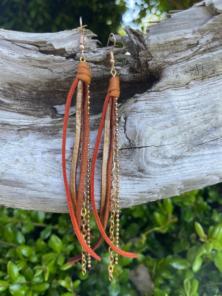 Brown and burnt orange colored suede with chain. description: these beautiful earrings have a distinctive design that uses length for movement and added dimension. hand crafted from colored suede and leather strips and beautiful thrifted necklace and bracelet chains, allow for a beautiful and fun up cycling. they come in different lengths ranging for 3" to 5" so there is a perfect fit for everyone. our goal is to create a unique piece of art that can cater to every style and add a little flare to everyday wear. Brown Jewelry With Adjustable Chain For Festival, Leather Dangle Jewelry For Party, Party Leather Dangle Jewelry, Trendy Leather Dangle Jewelry, Unique Brown Jewelry With Adjustable Chain, Brown Fringe Jewelry For Festivals, Orange Fringe Jewelry For Festivals, Handmade Rust Leather Jewelry, Brown Tassel Jewelry For Festivals