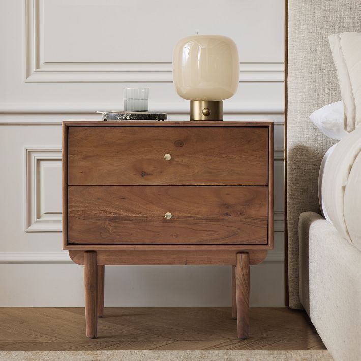 a nightstand with a lamp on top of it next to a bed