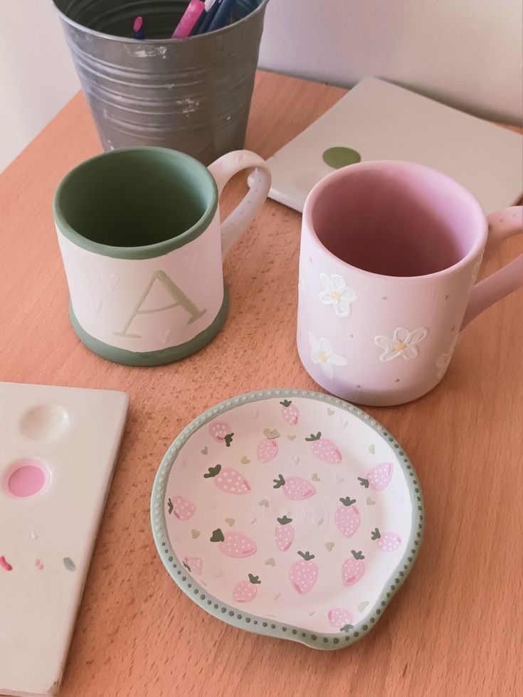 two mugs and a plate sitting on a table next to each other with pencils in them