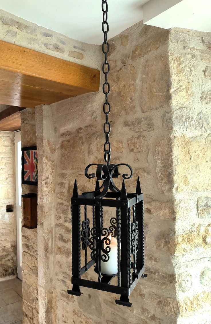 a lantern hanging from a stone wall with a candle in the center and an iron chain attached to it