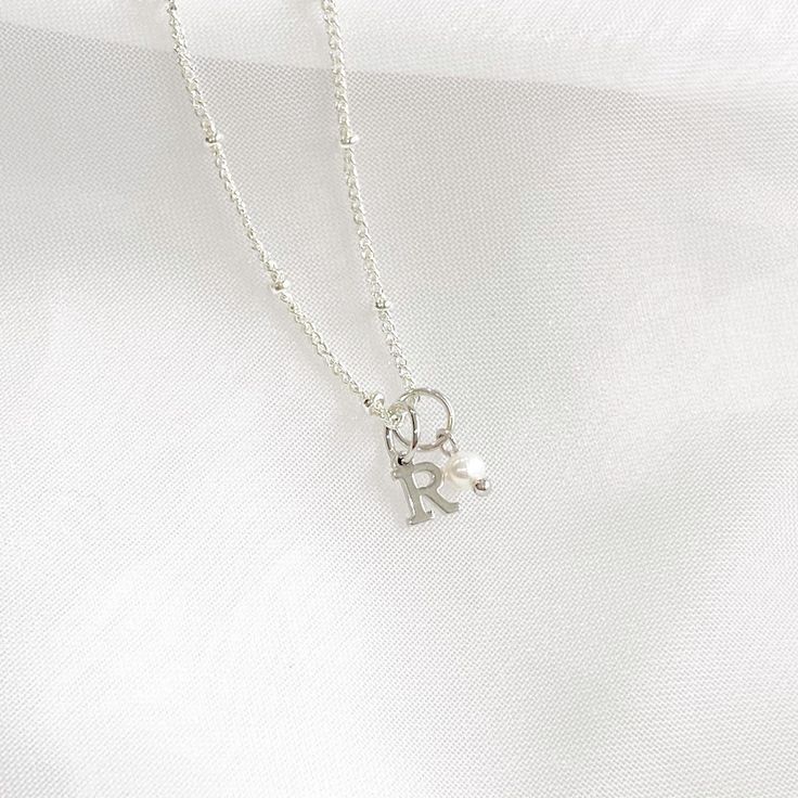 This stunning dainty letter necklace with pearl charm is perfect for anyone looking for understated elegance. The necklace features a delicate silver chain that holds a small, exquisite pearl charm and a capital letter of your choice.  ♡ Handcrafted in our Sydney Studio ♡ Natural Freshwater Pearl ♡ 925 Sterling Silver Plated ♡ Water Resistant ♡ 5mm Charm  PACKAGING: All of our items are carefully packed into a white jewellery box topped with a delicate white satin bow. Our shipping bags are beig Dainty Jewelry With Pearl Charm Initial Pendant, White Initial Pendant Charm Necklace With Delicate Chain, Silver Charm Necklace With Initial Pearl Pendant, Dainty Initial Pendant Charm Necklace For Her, Silver Initial Pendant Necklace With Pearl Charm, Silver Necklace With Initial Pendant And Pearl Charm, Initial Pendant Necklace With Pearl For Gift, Initial Necklace With Pearl Pendant For Gift, Dainty Initial Pendant Charm Necklace For Mother's Day