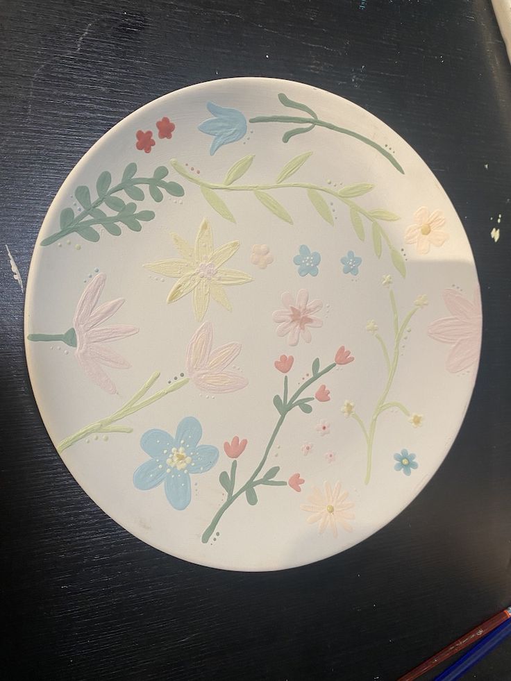 a plate with flowers painted on it sitting on a table next to some pencils