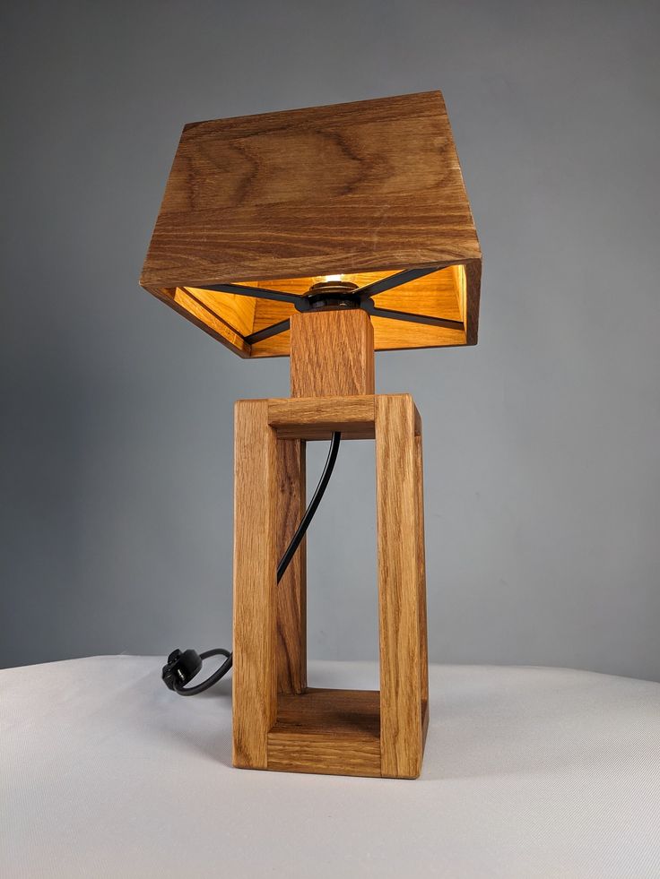 a wooden table lamp sitting on top of a white surface next to a black cord