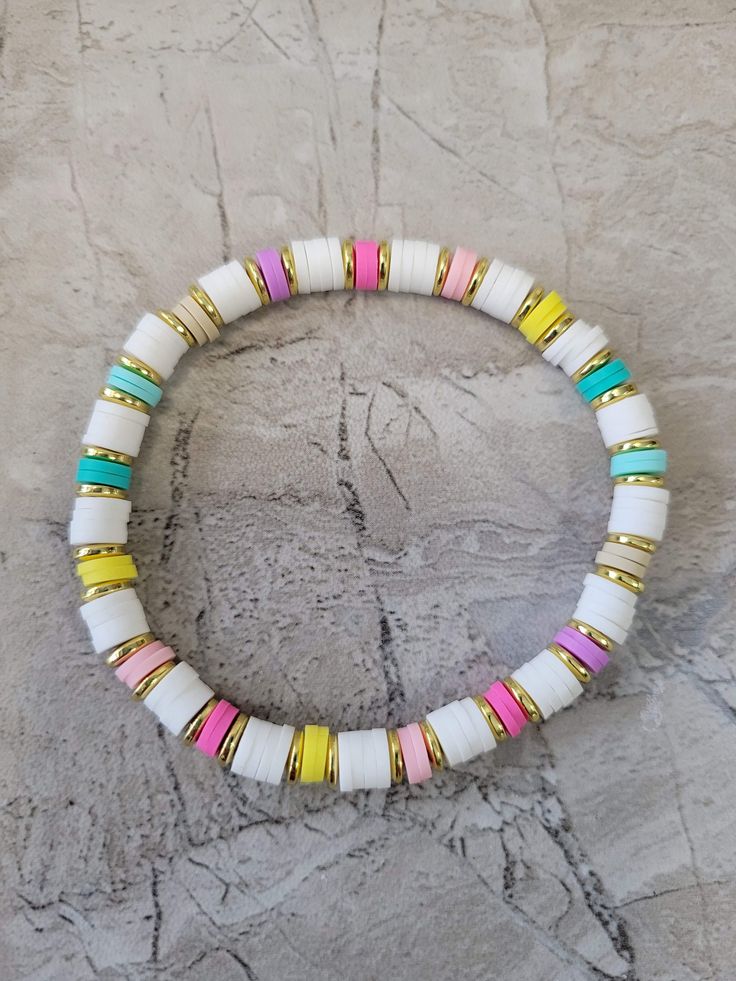 a white bracelet with multi colored beads on top of a stone wall next to a yellow and pink bead