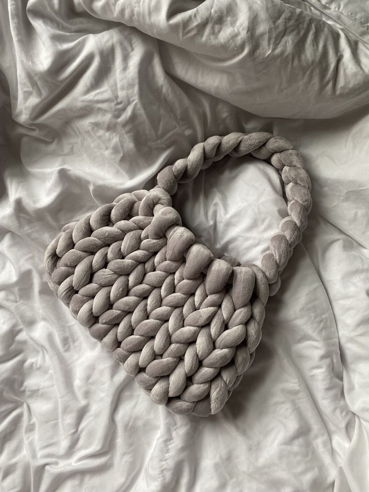 a handbag made out of pebbles on a white bed with sheets and pillows in the background