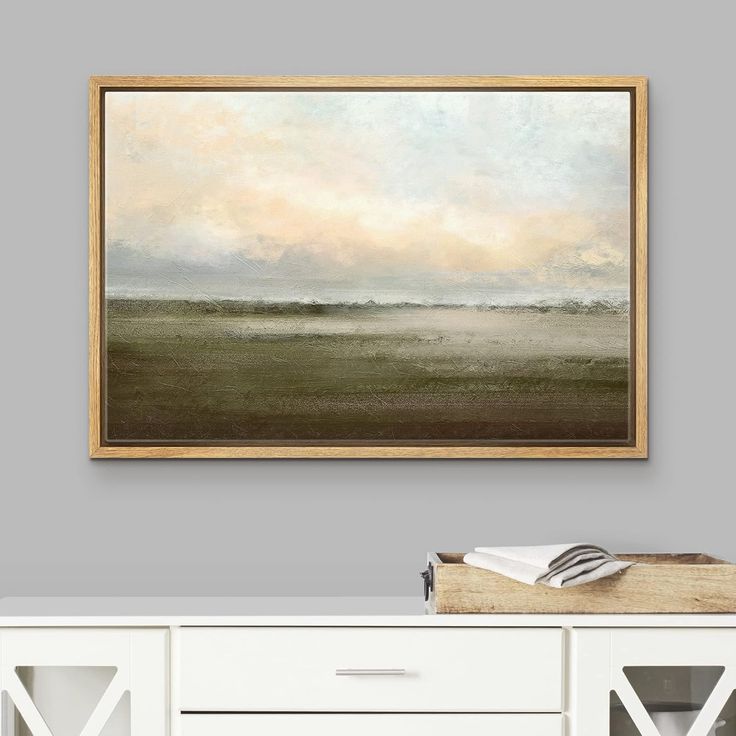 a painting hanging on the wall above a white dresser with drawers in front of it