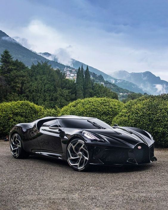 a black sports car parked on top of a parking lot next to bushes and trees