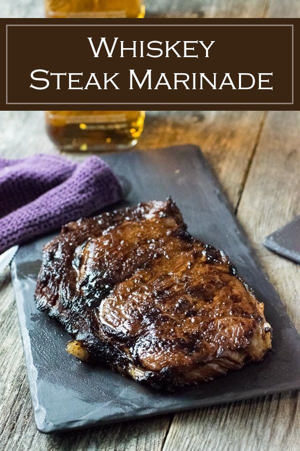 a steak on a slate plate next to a glass of whiskey and a purple napkin