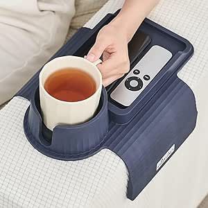 a person is holding a cup of tea while sitting on a bed with a remote control in their lap