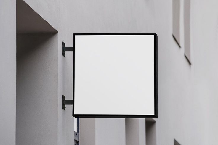 an empty sign hanging from the side of a building in front of a white wall