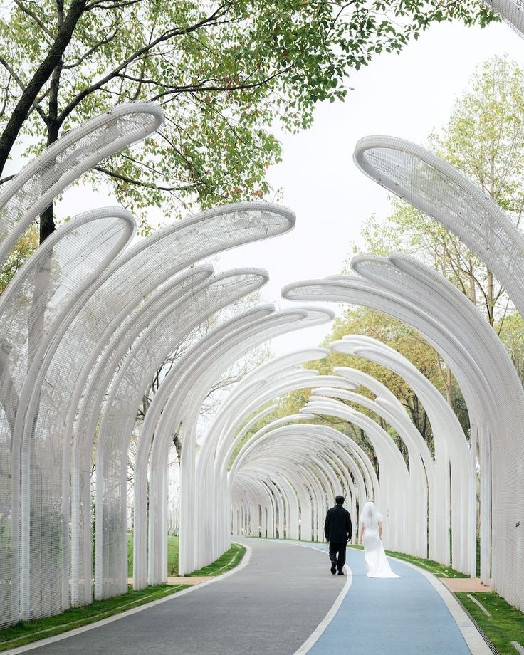 a man and woman are walking down the street in front of many white arches with trees on both sides