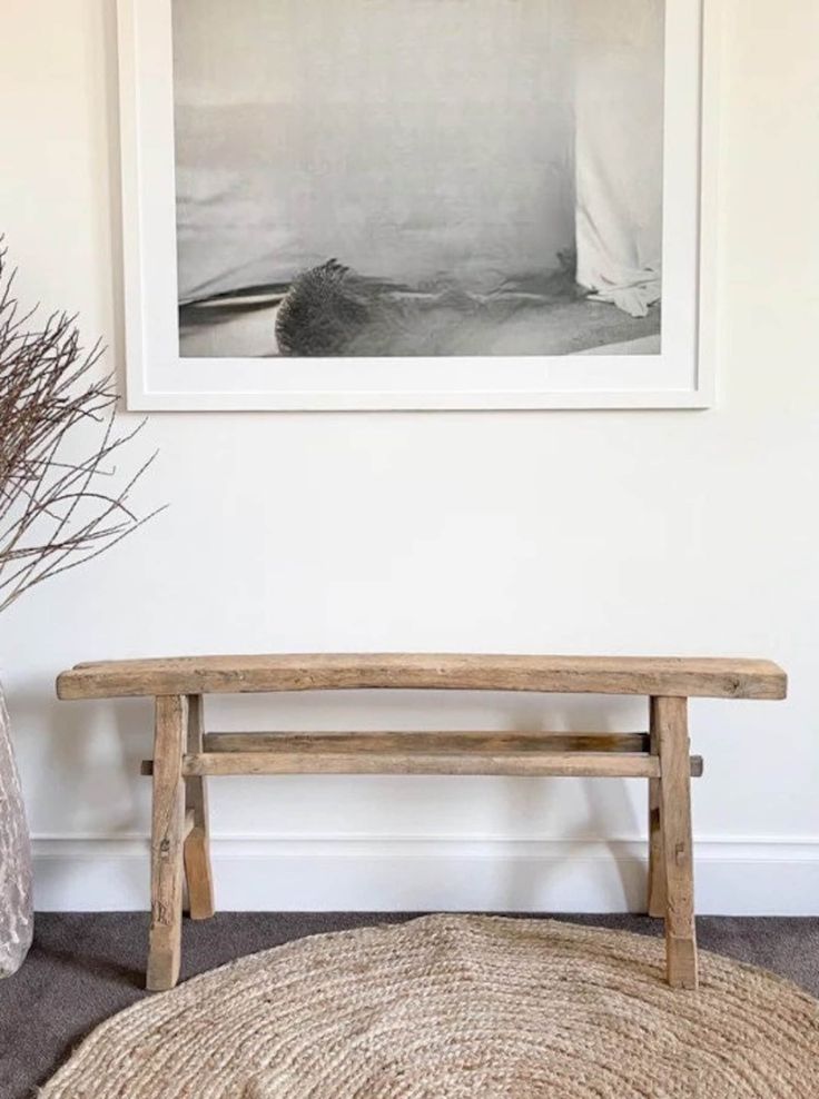 a wooden bench sitting next to a vase with flowers in it on top of a rug