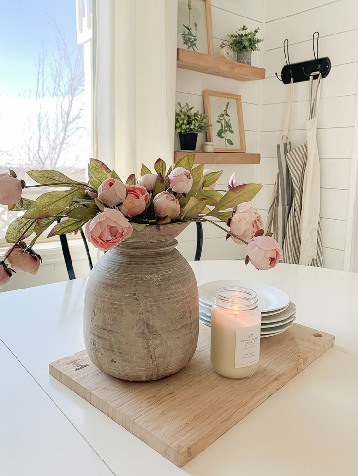 a vase filled with pink flowers sitting on top of a wooden table next to plates