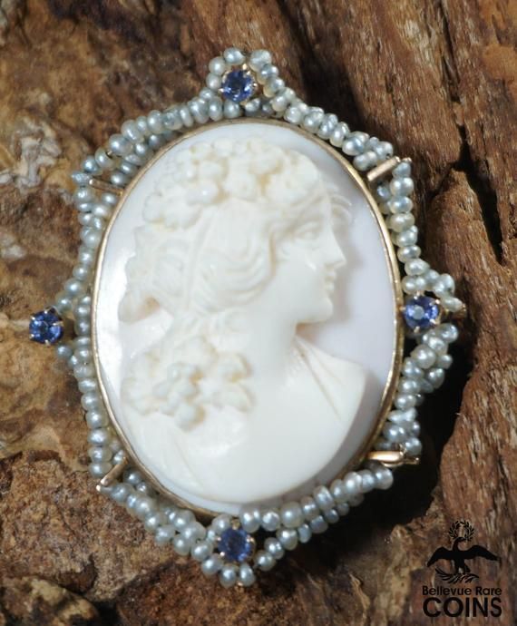 Metal: 10k Yellow Gold (.417)Weight: 8.4 gramsMeasurements: 1.25" Long; 1" Wide; 0.54" DeepMarkings: "10k"*This stunning brooch features a cameo of a finely dressed woman looking off to the right hand-carved on a pink/white shell, set into a 10k yellow gold border and bezel. The border features small pearls in two criss-crossed rows, with 4 small purple stones. The brooch features impressive high relief carving. The brooch also functions as a necklace pendant. This outstanding brooch is in great Oval Brooch Necklace For Wedding, Oval Brooch Necklaces For Wedding, Victorian White Cabochon Brooches, White Victorian Cabochon Brooches, Medallion Shaped Brooch For Wedding, Medallion Brooch Jewelry For Wedding, Wedding Medallion Brooch Jewelry, Victorian Brooch Jewelry For Memorial, Victorian Brooch For Memorial