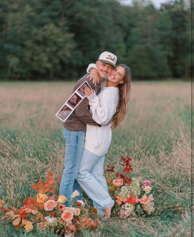 a man and woman hugging each other in a field with flowers on the ground behind them