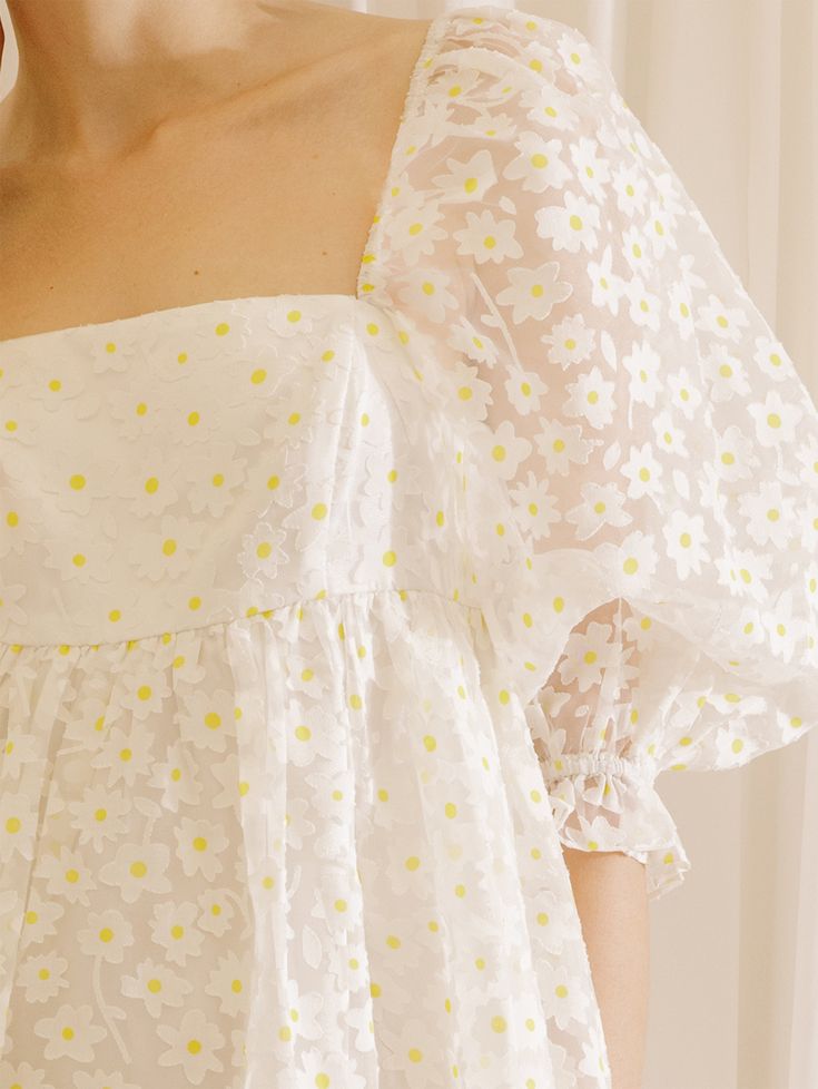 The Daisy Baby Doll Mini Dress is the perfect piece for those special bridal events this spring and summer. Featuring a detail white dress with a touch of yellow of Daisy print and a gathered empire waist, this elegant dress is made from sheer fabric with an underlined design for added coverage. With a back/front square neckline, bust darts, and oversized 3/4 puffy sleeves with ruffled cuffs, you'll feel comfy and stylish. Material:Cotton and Polyester Yellow Mini Dress For Spring Wedding, White Fitted Empire Waist Dress, Spring Wedding Yellow Mini Dress, White Smocked Bodice Mini Dress, Spring Mini Dress With Smocked Bodice And Empire Waist, Spring Empire Waist Mini Dress With Smocked Bodice, White Dress With Smocked Bodice And Square Neck, White Empire Waist Dress With Fitted Bodice, White Dress With Fitted Bodice And Empire Waist