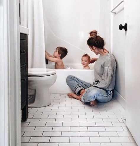 a woman sitting on the floor in front of a bathtub with two babies inside