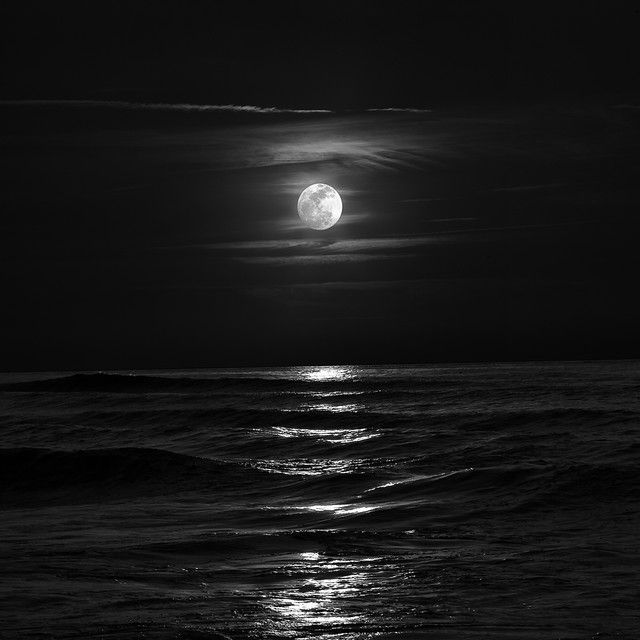 the moon is shining over the ocean in black and white