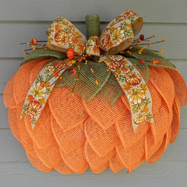 an orange mesh pumpkin hanging on the side of a house with a bow around it's neck