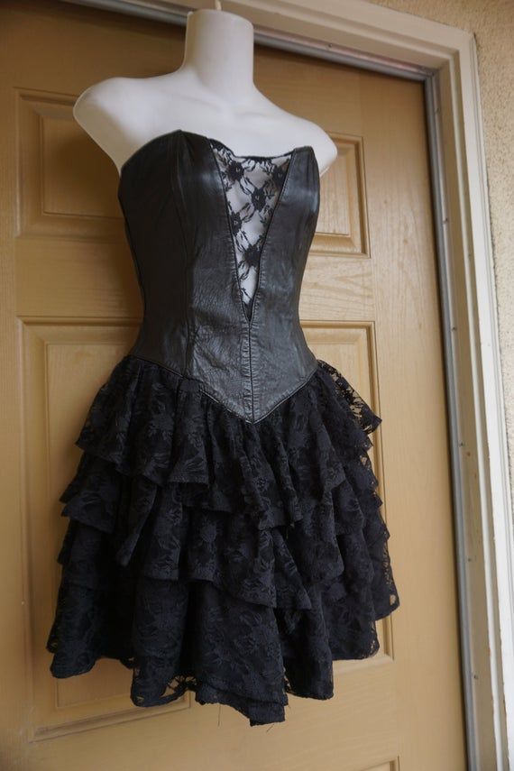 Vintage size small black dress with leather sweetheart bodice and ruffle lace layered skirt. Zips up the back. In good vintage condition but the puller on the zipper need to be reconnected somehow - see last photo. Measurements taken across front laid flat16" across front armpit to armpit12.5" across front of waist -doubles to 25"19" across front of hips26" length armpit to bottom Black Strapless Corset With Ruffles, Steampunk Lace Fitted Corset Dress, Fitted Lace Steampunk Corset Dress, Black Corset With Lace Trim And Fitted Bodice, Black Fitted Corset Dress With Ruffles, Black Ruffled Corset For Party, Steampunk Corset Dress For Parties, Steampunk Corset Dress For Party With Fitted Bodice, Black Lace Corset With Ruffles