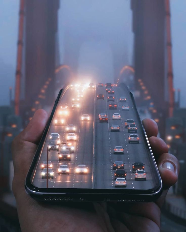 a person holding up a cell phone in front of a bridge with cars on it