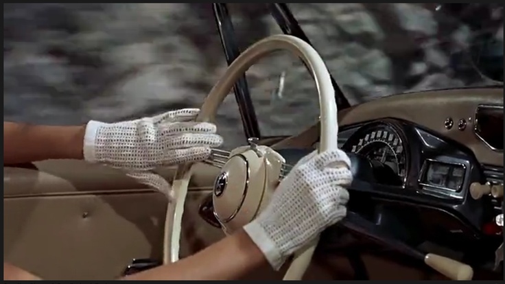 a person wearing white gloves sitting in a car holding the steering wheel with both hands