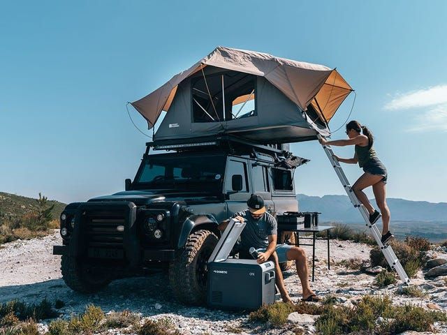 two people setting up a tent on top of a vehicle