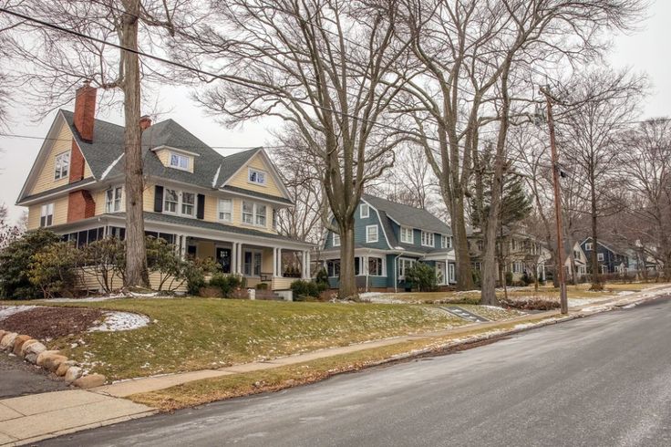 two story houses on the corner of a street with trees and grass in front of them