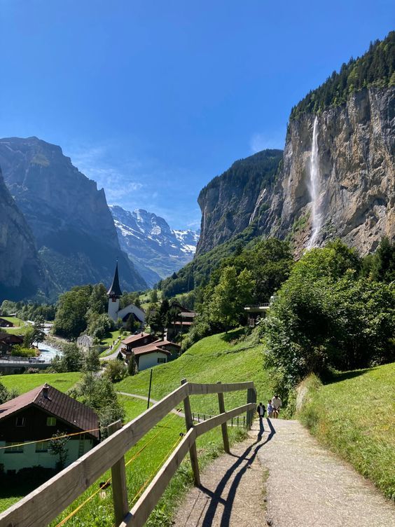 a wooden walkway leading up to a waterfall in the middle of a valley with green grass and trees on both sides