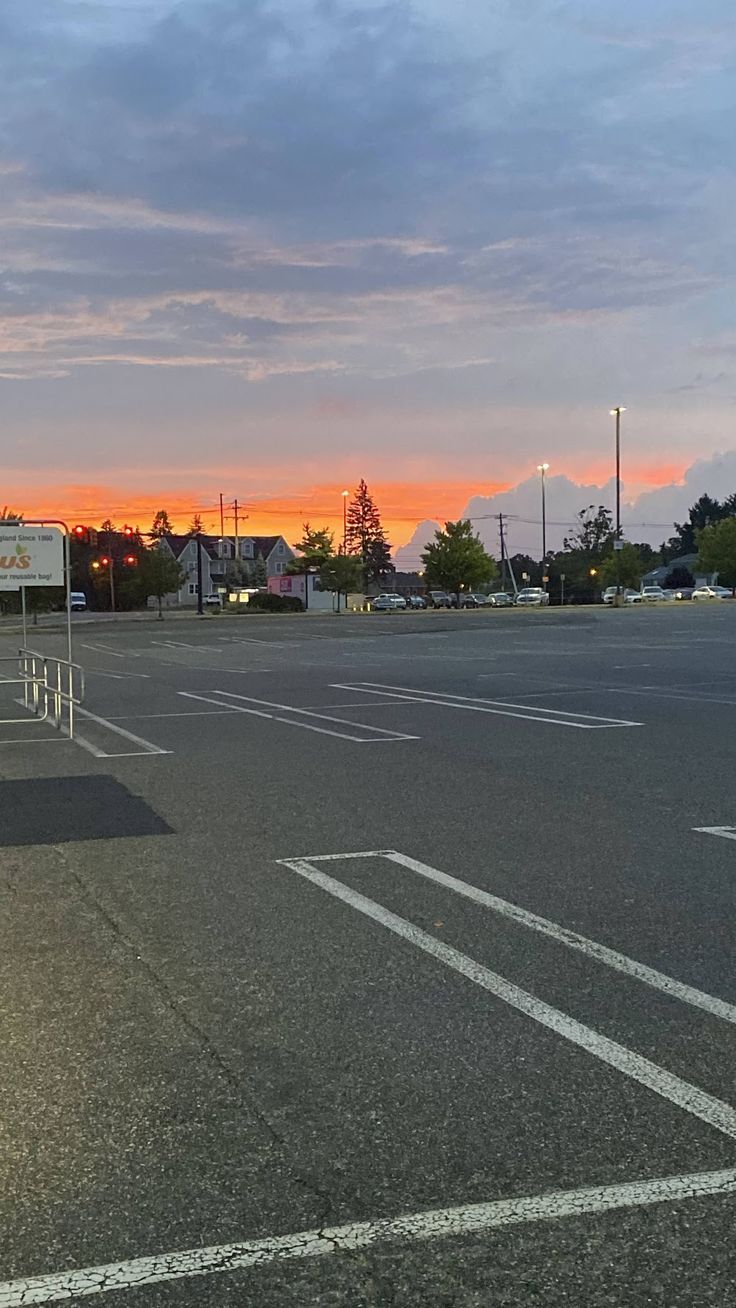 an empty parking lot at sunset with the sun setting in the distance and clouds above