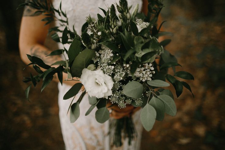 a woman holding a bouquet of flowers and greenery