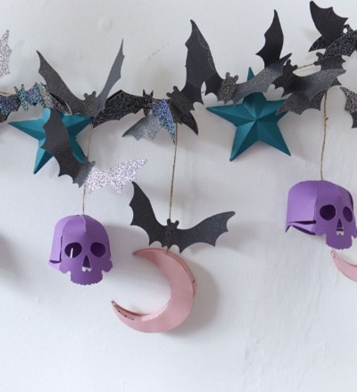 paper bats and skulls hanging from hooks on a white wall with pink moon, purple skull and star decorations