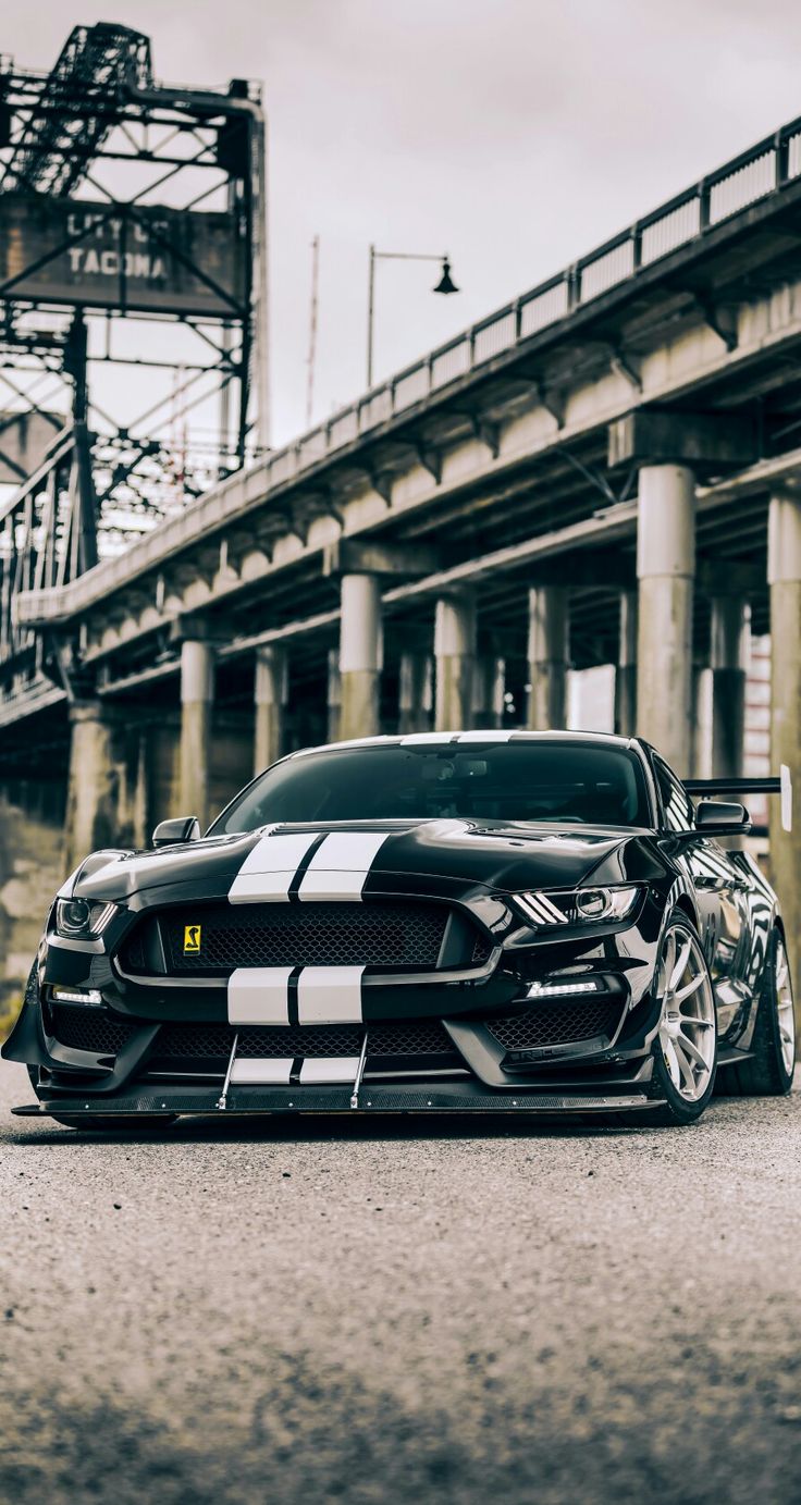 a black and white car parked in front of a building with an overpass behind it